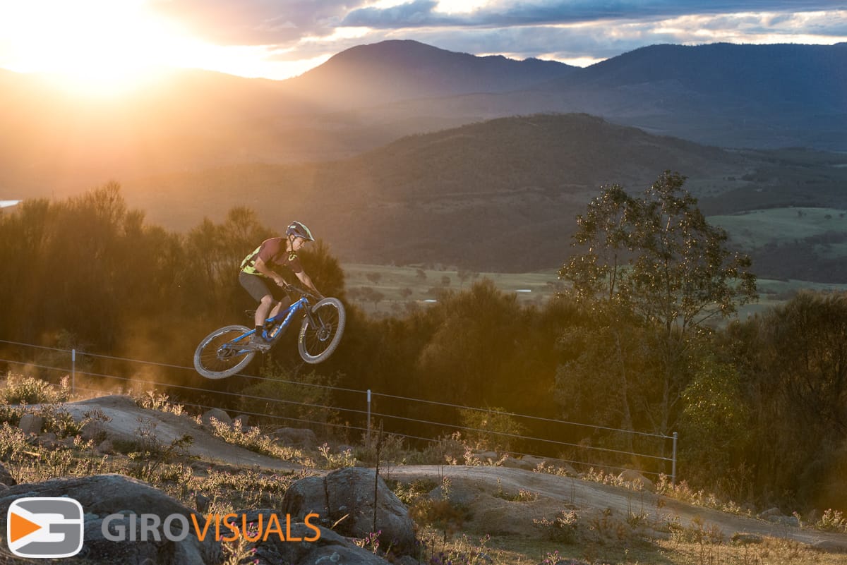 A mountain bike enduro rider jumps as the last of the day's sun lights the track.