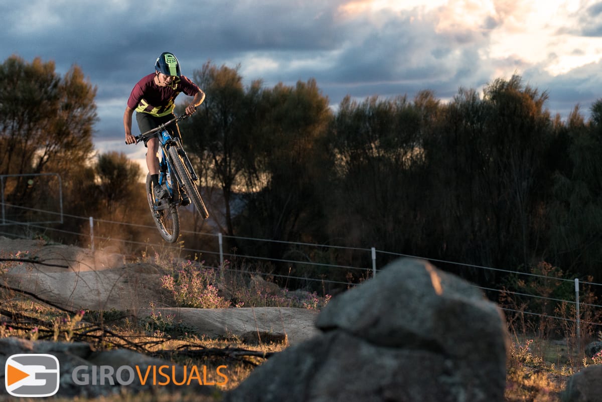 A mountain bike enduro rider jumps as the last of the day's sun lights the track.